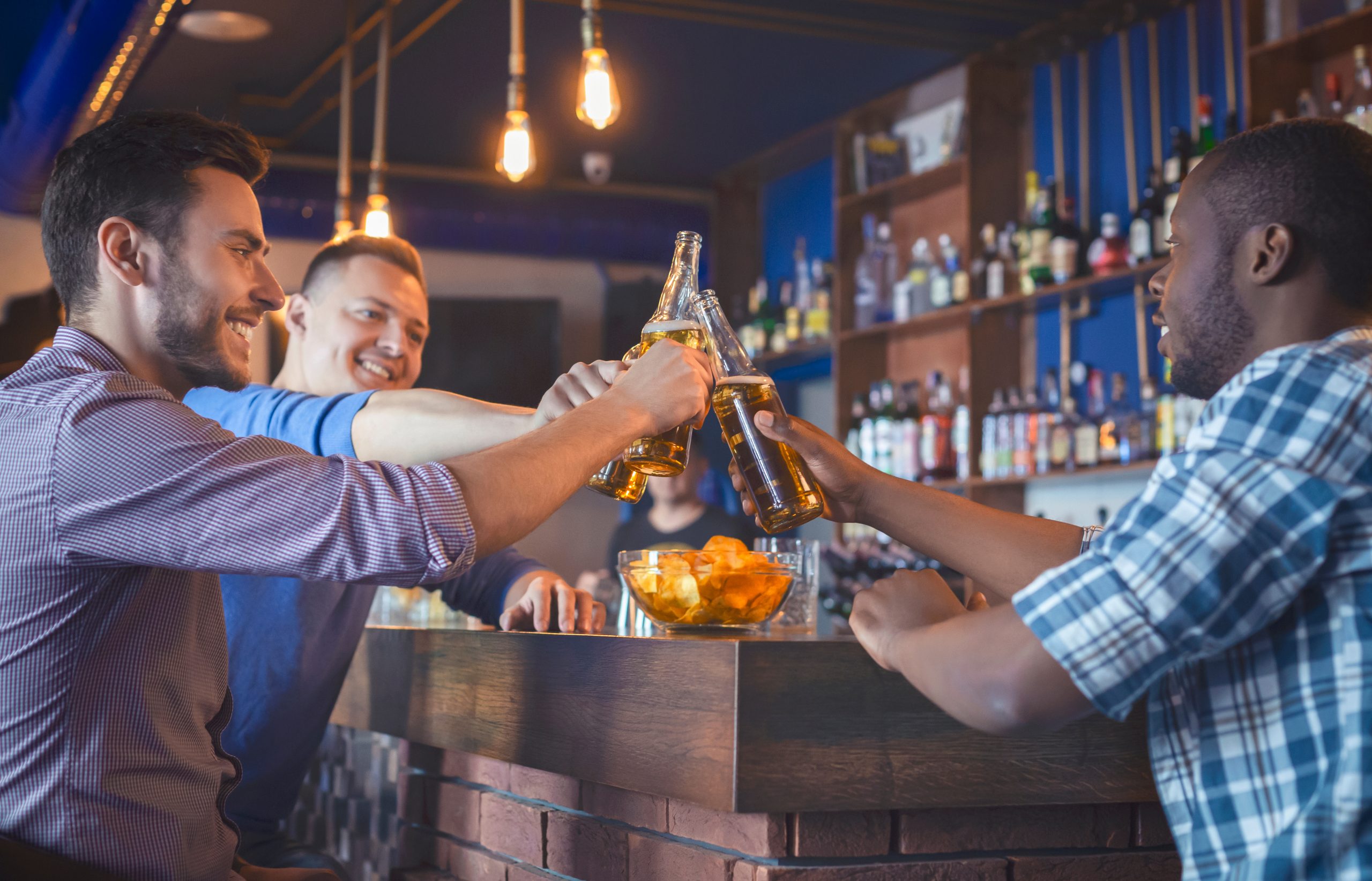 Happy Guys Clinking Beer Bottles In Bar